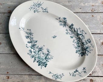 May include: Oval serving platter with a white background and a teal floral and bird design. The platter has a slightly raised edge and is decorated with detailed botanical illustrations and small birds.