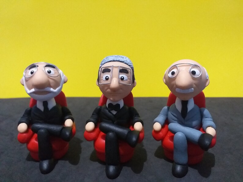 May include: Three small figurines of men wearing suits and glasses, sitting in red chairs. The men have grey hair and are smiling.