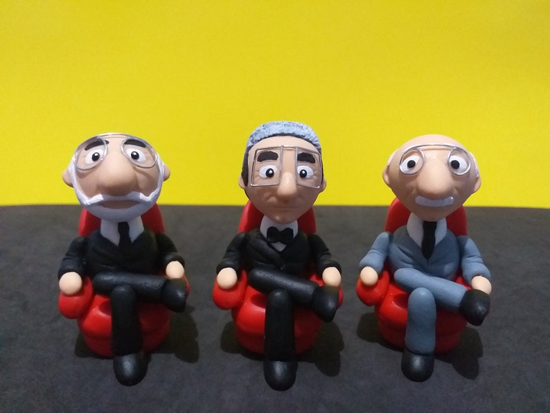 May include: Three small figurines of men wearing glasses and sitting in red chairs. The men are wearing different outfits, including a suit, a tuxedo, and a grey suit.