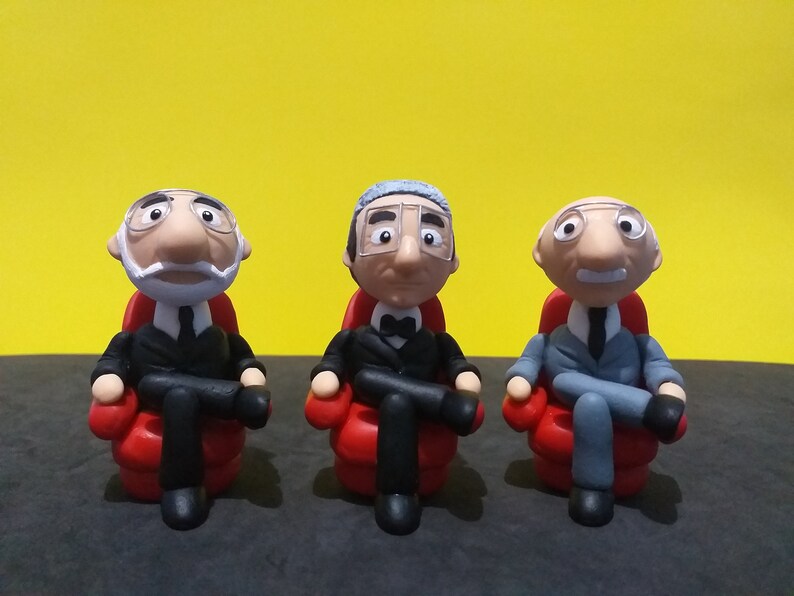 May include: Three figurines of men wearing suits and glasses, sitting in red chairs. The men have white hair and different facial expressions.