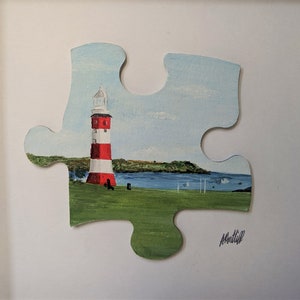 Pu&ograve; includere: Un dipinto di un faro rosso e bianco su una collina verde erbosa con uno specchio d'acqua blu sullo sfondo. Il dipinto &egrave; su un pezzo di puzzle.