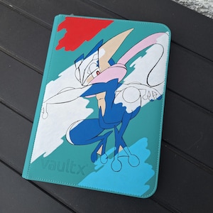 May include: A teal Vault X binder featuring a stylized illustration of a blue and white character with pink and tan accents. The artwork is set against a backdrop of teal, white, red, and blue brushstrokes. The Vault X logo is visible.