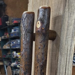 May include: Two rustic wooden door handles, made from tree branches, are mounted on a light-coloured wooden slab. The handles are dark brown with visible knots and bark texture, adding a natural, organic aesthetic.