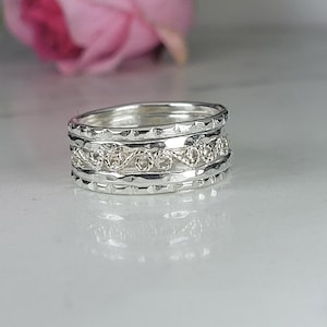 Może przedstawiać: Srebrny pierścionek z szeroką obręczą, ozdobiony wieloma warstwami skomplikowanych wzorów. Pierścionek ma fakturowane, młotkowane wykończenie i delikatny, tkany wzór.