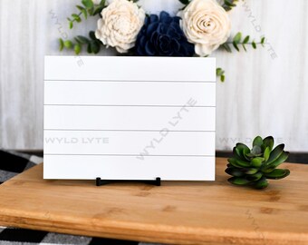 May include: White wooden sign with five horizontal lines, standing on a black easel. The sign is on a wooden cutting board with a small green succulent plant to the right.