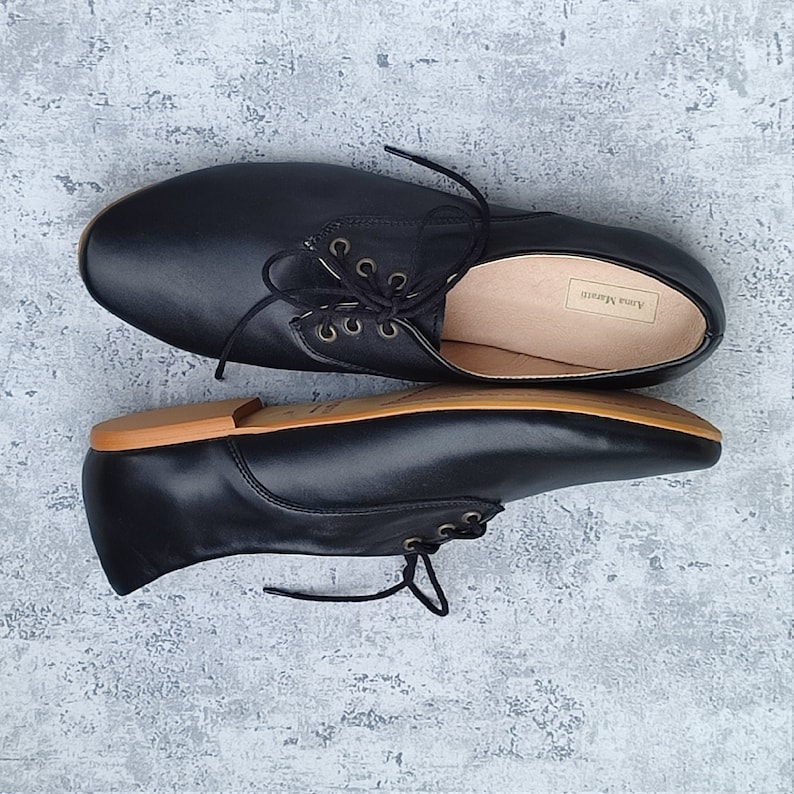 K&ouml;nnte beinhalten: Ein Paar schwarze Lederschn&uuml;rschuhe mit brauner Sohle. Die Schuhe haben eine abgerundete Spitze und einen niedrigen Absatz. Der Markenname "Anna Karen" ist auf der Innenseite eines Schuhs sichtbar.