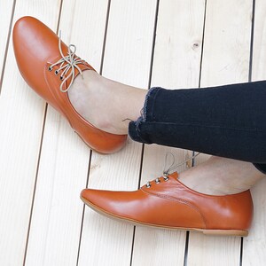 K&ouml;nnte beinhalten: Ein Paar braune Lederschn&uuml;rschuhe mit spitzer Zehenpartie. Die Schuhe werden von einer Person getragen, die eine schwarze Jeans tr&auml;gt.