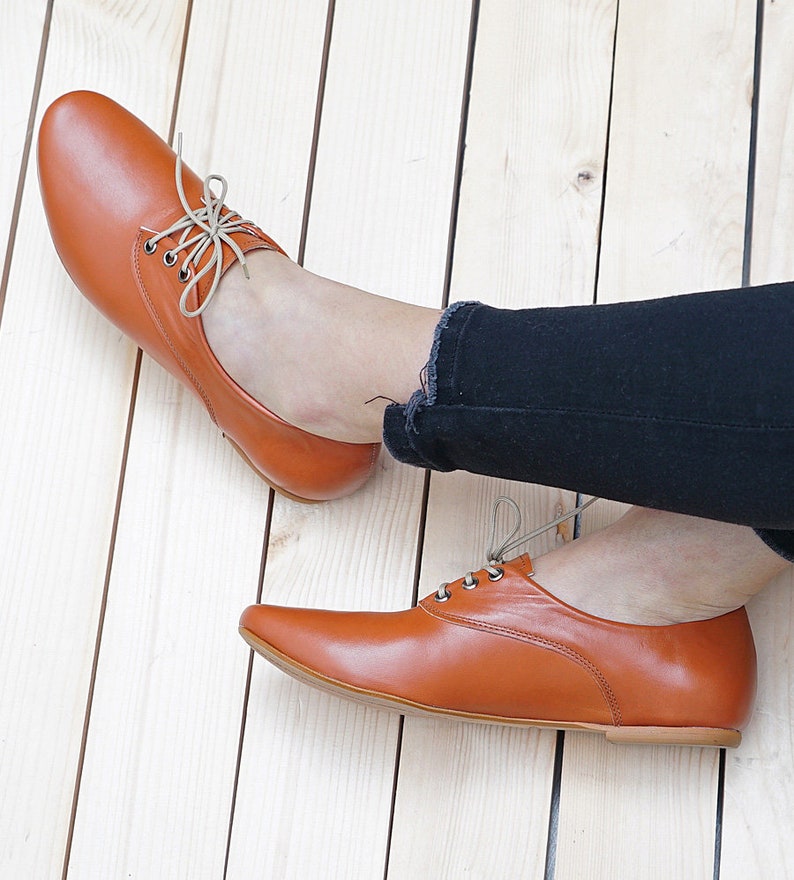K&ouml;nnte beinhalten: Ein Paar braune Lederschn&uuml;rschuhe mit spitzer Zehenpartie. Die Schuhe werden von einer Person getragen, die eine schwarze Jeans tr&auml;gt.