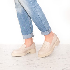 May include: A pair of light beige leather loafers with a chunky platform sole. The loafers have a simple design with a small buckle detail on the front.