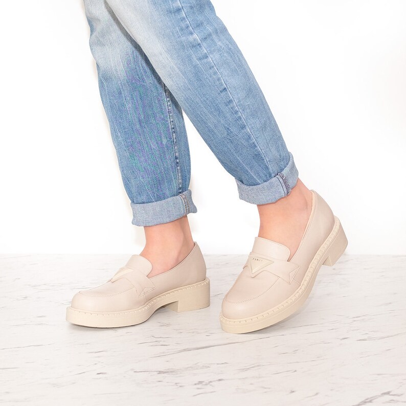 May include: A pair of light beige leather loafers with a chunky platform sole. The loafers have a simple design with a small buckle detail on the front.