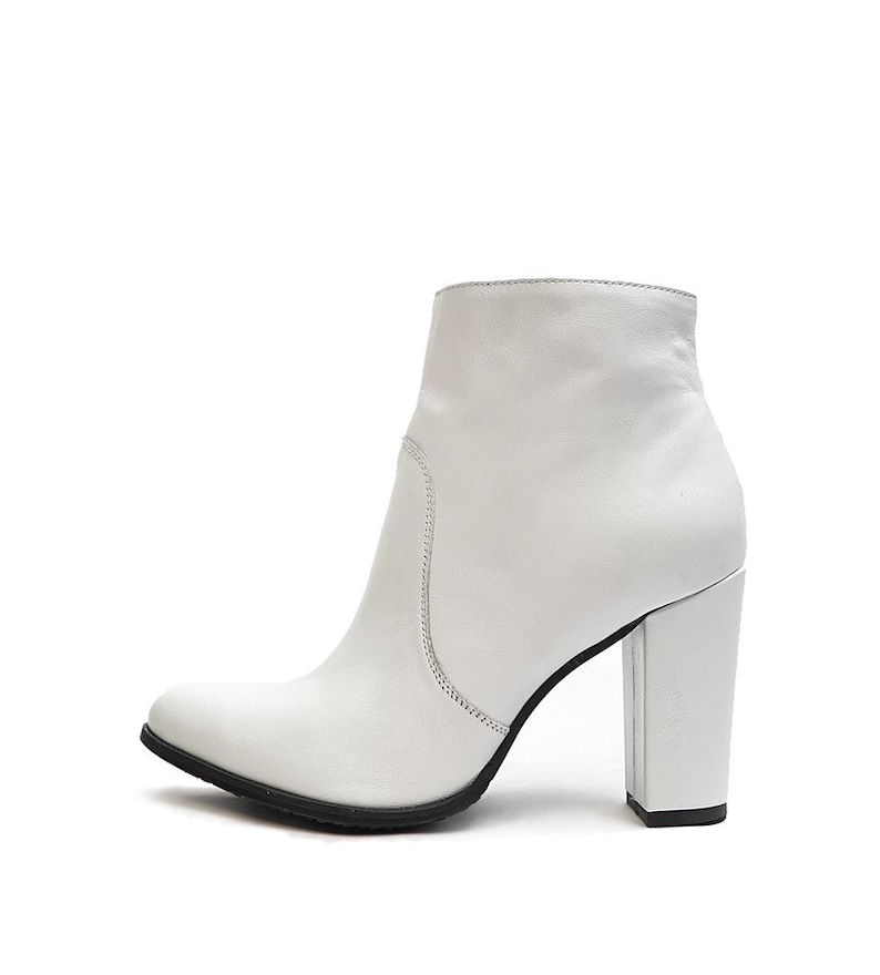 May include: White leather ankle boots with a block heel. The boots have a pointed toe and a zipper on the back.