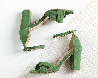Könnte beinhalten: Ein Paar grüne Wildledersandalen mit Fersen und Knöchelriemen. Die Sandalen haben ein geknotetes Detail am vorderen Riemen und einen Blockabsatz.