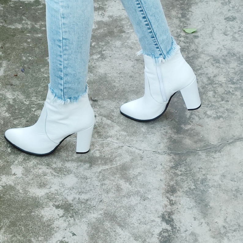 May include: White ankle boots with a block heel and a pointed toe. The boots are made of leather and have a zipper on the side.