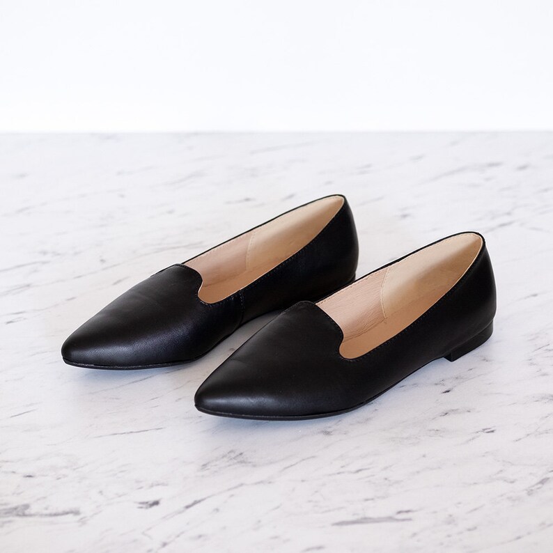Op de afbeelding: Een paar zwarte, spitse ballerina's van leer met een slip-on ontwerp. De schoenen hebben een eenvoudige, minimalistische stijl.