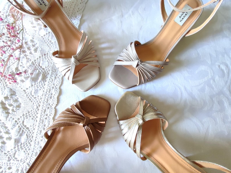 May include: Four pairs of women's sandals in various neutral tones. The sandals feature thin straps, open toes, and decorative knotted details. The soles are a light tan color, and the heels are low. The sandals are arranged on a white surface.