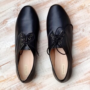 K&ouml;nnte beinhalten: Ein Paar schwarze Lederschn&uuml;rschuhe mit abgerundeter Spitze. Die Schuhe haben ein schlichtes Design und sind aus weichem, geschmeidigem Leder gefertigt. Der Markenname "Anna Marchetti" ist auf der Innenseite jedes Schuhs aufgedruckt.