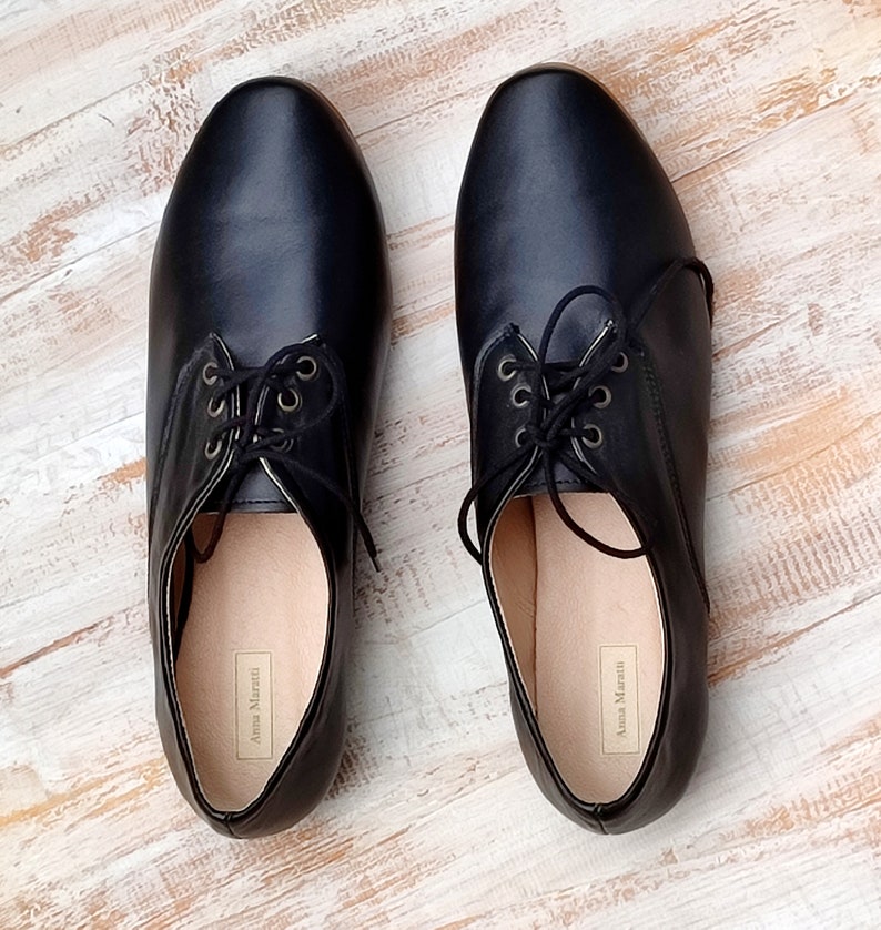 K&ouml;nnte beinhalten: Ein Paar schwarze Lederschn&uuml;rschuhe mit abgerundeter Spitze. Die Schuhe haben ein schlichtes Design und sind aus weichem, geschmeidigem Leder gefertigt. Der Markenname "Anna Marchetti" ist auf der Innenseite jedes Schuhs aufgedruckt.