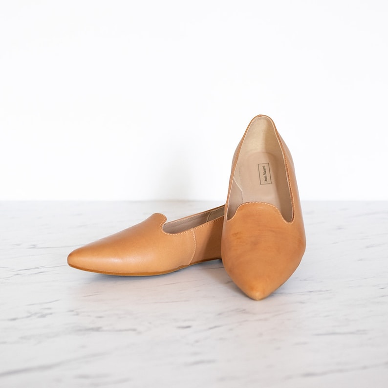 Op de afbeelding: Een paar spitse ballerina's van bruin leer. De schoenen hebben een simpel ontwerp en zijn gemaakt van zacht, soepel leer.