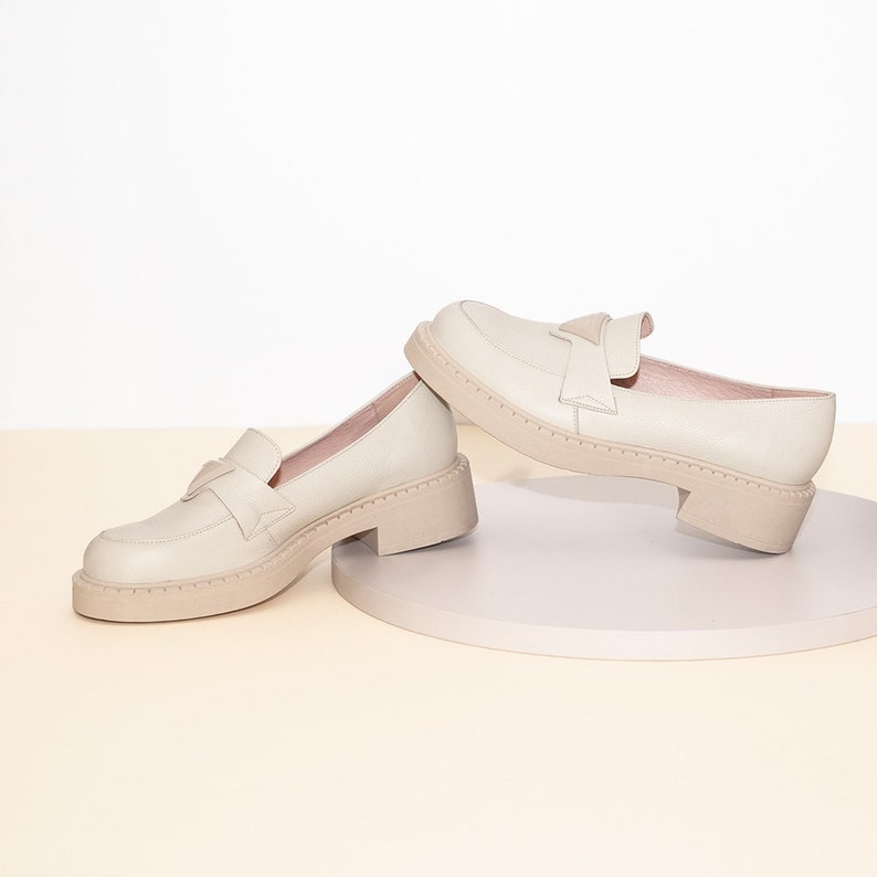 May include: A pair of off-white leather loafers with a chunky platform sole. The loafers have a simple design with a single strap across the top.