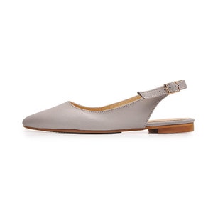 Könnte beinhalten: Ein Paar graue Lederslingbacks mit goldener Schnalle. Die Schuhe haben eine spitze Zehenpartie und einen niedrigen Absatz.