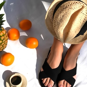 Pode incluir: Um chap&eacute;u de palha, sand&aacute;lias pretas e laranjas est&atilde;o dispostos sobre uma superf&iacute;cie branca. Uma x&iacute;cara de caf&eacute; e um prato com fatias de laranja tamb&eacute;m est&atilde;o presentes. Um abacaxi &eacute; vis&iacute;vel ao fundo, sugerindo um piquenique de ver&atilde;o.