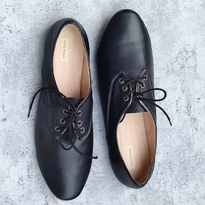K&ouml;nnte beinhalten: Ein Paar schwarze Lederschn&uuml;rschuhe mit goldenen &Ouml;sen. Die Schuhe haben eine spitze Zehenpartie und einen niedrigen Absatz. Der Markenname "Anna Marani" ist auf der Innenseite der Schuhe sichtbar.