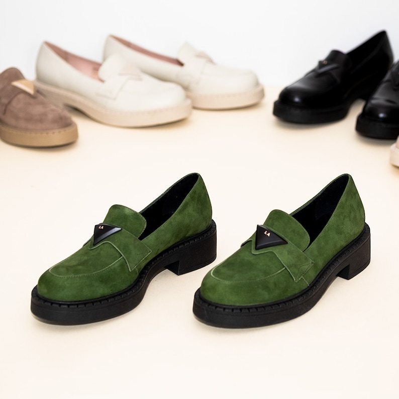 May include: A pair of green suede loafers with black soles and a gold triangle logo. The loafers have a chunky platform heel.
