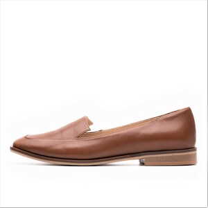 Pu&ograve; includere: Una scarpa mocassino in pelle marrone con punta quadrata e tacco basso. La scarpa ha una texture liscia e un design classico, adatta a varie occasioni. La suola &egrave; di colore marrone chiaro.