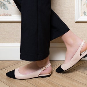 May include: A pair of light pink leather slip-on shoes with black toe caps and a black strap around the ankle.