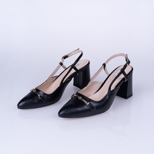 May include: A pair of black leather heeled shoes with a gold buckle detail. The shoes have a slingback strap and a pointed toe.