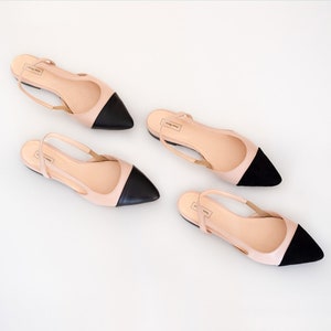 May include: Four pairs of ballet flats with a pointed toe and slingback strap. The shoes have a light pink body with a black toe cap. The brand name "Anna Mary" is printed on the insole.