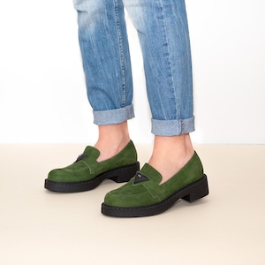 May include: Green suede loafers with a black platform sole and a black triangular accent on the front.