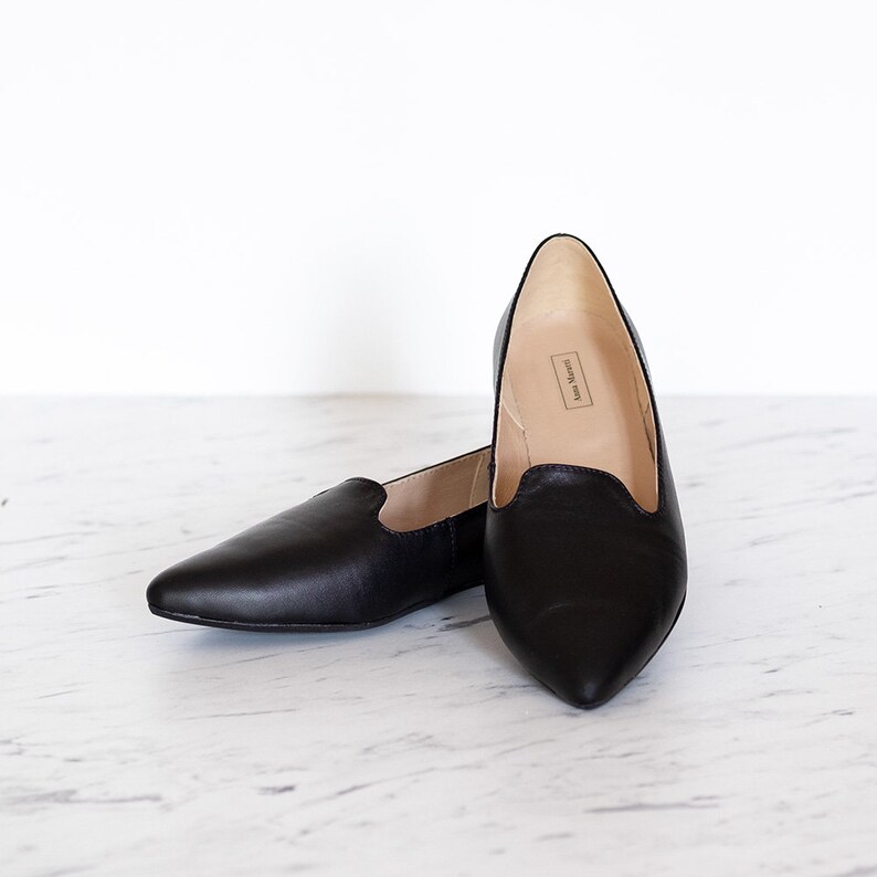 Op de afbeelding: Een paar zwarte, spitse ballerina's van leer. De schoenen hebben een simpel ontwerp en zien er comfortabel uit.