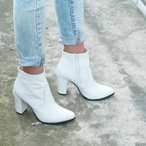 May include: White leather ankle boots with a block heel and a zipper up the back. The boots are worn with light blue jeans.