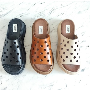 May include: Three pairs of black, brown, and beige leather sandals with a polka dot pattern. The sandals have a thick platform sole and are labeled "Anna Maratti" on the strap.