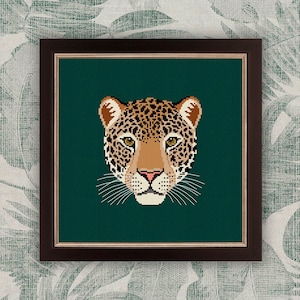 May include: A framed print of a jaguar's face on a dark green background. The jaguar has brown and black spots and a white muzzle.