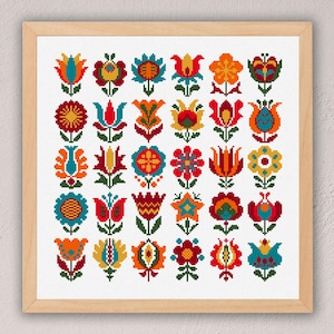 May include: A square wooden frame containing a white fabric piece with a grid of thirty colourful cross-stitch flower motifs. The flowers are arranged in five rows and six columns, featuring vibrant red, orange, yellow, blue, and green thread.