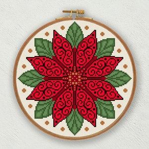 May include: A red poinsettia flower with green leaves and gold accents is embroidered on a white canvas in a round wooden embroidery hoop.