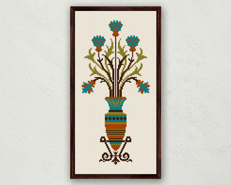 May include: A framed cross-stitch embroidery featuring a stylized vase with blue flowers and green leaves. The vase is decorated with brown, orange, and blue geometric patterns.