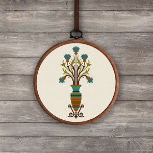 May include: A cross-stitch embroidery hoop with a design of a vase with blue flowers and green leaves. The vase is decorated with brown, orange, and blue stripes.