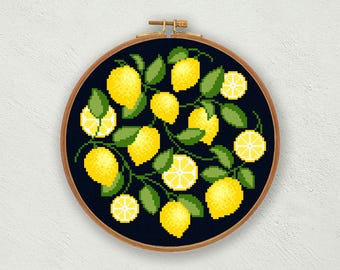May include: A circular wooden embroidery hoop containing a cross-stitch pattern on dark navy fabric. The design features bright yellow whole lemons and sliced lemon segments interspersed with green leaves on thin brown stems.