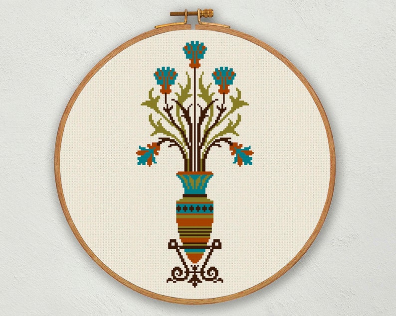 May include: A cross-stitch embroidery design of a vase with blue flowers and green leaves. The vase is brown and orange with a blue and white pattern. The design is framed in a wooden hoop.