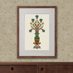 May include: A framed cross-stitch embroidery of a stylized vase with blue flowers and green leaves. The vase is brown, orange, and blue with a geometric pattern.