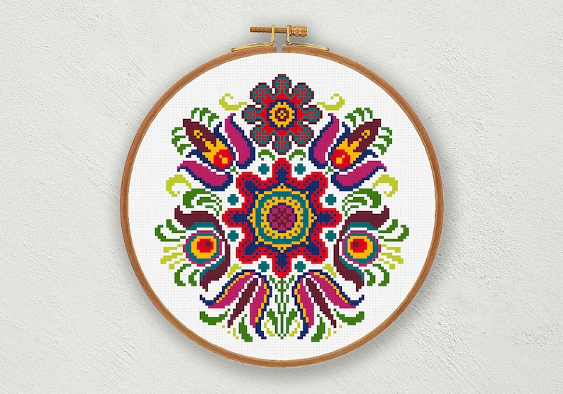 Puede incluir: Un patr&oacute;n de bordado floral colorido con una flor central en tonos de rojo, azul, amarillo y verde. El dise&ntilde;o est&aacute; rodeado de flores y hojas m&aacute;s peque&ntilde;as en una variedad de colores.