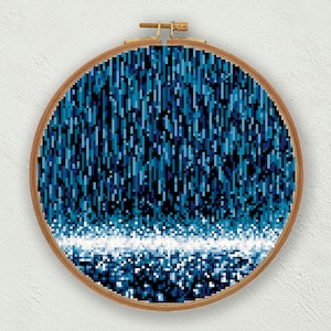 May include: A blue and white pixelated design of a waterfall in a round wooden embroidery hoop.