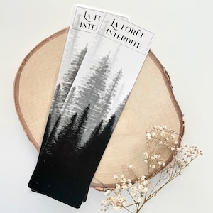 May include: Two bookmarks with a black and white forest design. The bookmarks have the text "LA FOR&Ecirc;T INTERDITE" at the top. The bookmarks are on a wooden slice with small white flowers.