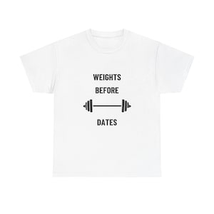 May include: White t-shirt with the text "WEIGHTS BEFORE DATES" in black, with a barbell graphic. The shirt is a crew neck and appears to be made of cotton or a similar fabric. The design is centered on the front of the shirt.