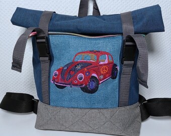 Könnte beinhalten: Ein blauer Jeans-Rucksack mit einem grauen gesteppten Boden. Der Rucksack hat ein großes gesticktes Bild eines roten Volkswagen Käfers mit einem Peace-Zeichen an der Heckscheibe.
