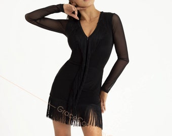 May include: A black dance dress with a fringe trim and long sleeves. The dress has a V-neckline and a zipper closure. The model is wearing the dress with brown heels.