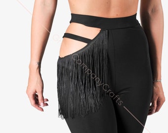 May include: Black leggings with a high waist and fringe detail. The leggings have cut-out accents on the side and a long fringe that hangs down the leg. The outfit is completed with a black velvet crop top.